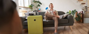 Yakışıklı genç adam kanepede bavuluyla oturuyor, elinde akıllı telefon, kitap pansiyonu ya da tatil tatili var, cep telefonuyla sohbet ediyor. Turizm ve seyahat kavramı