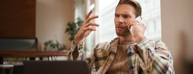 Telefonda biriyle tartışan kafası karışmış bir adamın portresi, iş adamı projeyi tartışıyor, dizüstü bilgisayardaki çizelgeye bakıyor, arama yapmak için cep telefonu kullanıyor, hayal kırıklığıyla monitöre bakıyor..