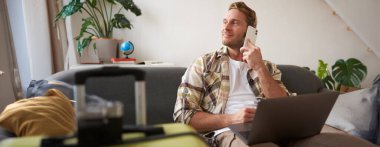 Bilgisayarlı yakışıklı bir adam, bir telefon görüşmesi yapıyor, telefonda beklerken yan tarafa bakıyor, internetten rezervasyon yaptığını doğruluyor. Turizm konsepti