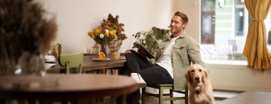 Yakışıklı genç adamın portresi köpeğiyle kafede oturuyor Golden Retriever 'ı okşuyor, tabletten haberler okuyor, bir fincan kahveyle rahatlıyor..