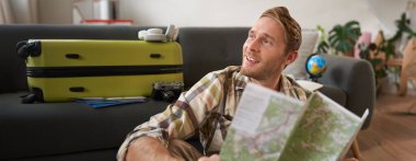 Yakışıklı, gülümseyen bir turist, elinde harita olan bir adam, tatilini planlıyor, tatile çıkıyor, rüya gibi, mutlu bir yüz ifadesi takınıyor. Seyahat, insan ve turizm konsepti