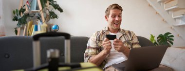 Mutlu adam portresi, gezgin, kredi kartı tutan ve dizüstü bilgisayar kullanan, tatil rezervasyonu yapan, yaz tatili için internetten bilet alan,.