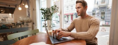 Ciddi görünümlü kafe sahibi, dizüstü bilgisayarda çalışan yakışıklı adam, kahve dükkanına gelen ziyaretçi, e-posta gönderen, klavyesinde yazan..