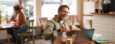 Genç gülümseyen adamın portresi, çevrimiçi öğretmen dizüstü bilgisayarda baş parmak gösteriyor, iyi iş çıkarmış biriyle görüntülü konuşmalar, adam onaylıyor..