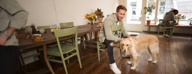 Güzel köpeğiyle evcil hayvan dostu kafede oturan yakışıklı bir adamın hayat tarzı portresi Golden Retriever 'ı okşuyor ve bir emir bekliyor..