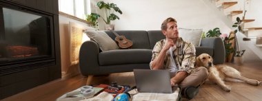 Köpekli bir adamın portresi, yerde oturuyor, bavul ve dizüstü bilgisayarı açık, internetten rezervasyon yaptırıyor veya alıyor, tatil planları yapıyor, tatile hazırlanıyor..