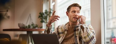 Telefonda konuşan ciddi iş adamının portresi, bir kafede dizüstü bilgisayarla oturmak, proje üzerinde çalışmak, telefonda işle ilgili konuları tartışmak,.