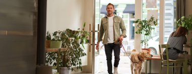 Yakışıklı bir genç adam tasmalı köpeğiyle kafeye giriyor, hayvan dostu kahve dükkanına giriyor, kapıyı açıyor..