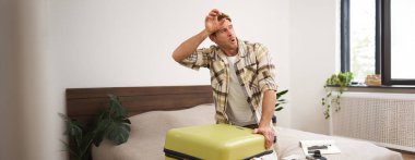 Terleyen genç adamın portresi, bavulunu kapatması, bir sürü kıyafetle valizi kapatmaya çalışması, yatağa oturması, yaz tatili için eşyalarını toplaması, ya da iş seyahatine çıkması..