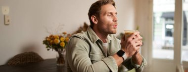 Kafedeki yakışıklı sakallı adamın portresi, sandalyede oturuyor, cappuccino içiyor, kafede dinleniyor..