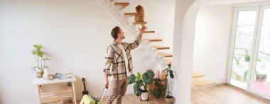 Bavullu gülümseyen adamın dikey görüntüsü, kediyle oynayan, ayakta duran ve bavul taşıyan. Halk konsepti