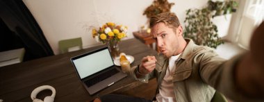 Ciddi bir adamın portresi yumruğu ve tehditkar yüzüyle selfie çeker, kafede oturur, kahve dükkanında dizüstü bilgisayar ve bir bardak kahveyle poz verir..