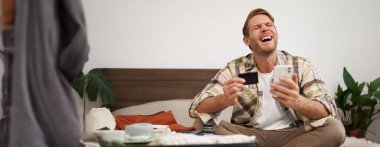 Neşeli erkek turist, bavul hazırlayan adam, biletleri kredi kartı ve akıllı telefon uygulaması ile ödüyor, kutluyor, tatile gitmek için heyecanlı..