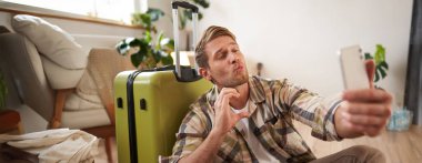 Yakışıklı, gülümseyen bir adam öpüşen yüzünü ve kalp işaretini gösterir, tatile gider, cep telefonu uygulamasında selfie çeker. Turizm ve seyahat kavramı