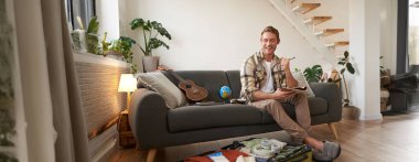 Kalemi ve defteri olan mutlu bir adam, seyahat için eşya listesi ve bavul hazırlıyor, tatile çıkıyor, yaz tatiline hazırlanıyor, oturma odasında oturuyor..