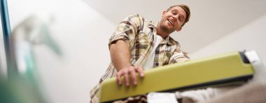 Kaslı, güçlü bir gencin alt açılı portresi. Elbiseleriyle dolu valizini kapatmaya çalışıyor. Çantasına gayretle bastırıyor. Turizm ve yaz tatili konsepti