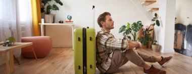 Yakışıklı genç bir adamın portresi, bavuluyla oturan bir turist, elinde pasaport ve uçak biletleri, tatile çıkıyor..