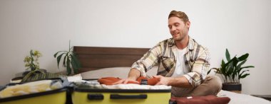 Gülümseyen yakışıklı bir adamın portresi, yatağa oturur, bavuluna kıyafet koyar, tatile gider, tatille ilgili rüyalar görür, seyahat acentasıyla seyahat eder ve eşyalarını toplar. Yaşam tarzı ve turizm konsepti