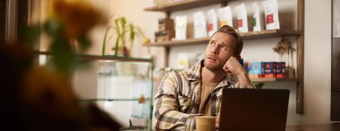 Bir kahve dükkanında uzaktan çalışırken konsantre olmuş gibi görünen bir adam. Kafe sahibi laptopuyla oturmuş, kapuçino içiyor, düşünceli bir yüz ifadesiyle yan gelip bakıyor, ilham alıyor..