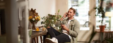 Yakışıklı, mutlu genç bir adamın portresi, bir kafede dinleniyor, kablosuz kulaklıkla müzik dinliyor, akıllı telefon tutuyor, en sevdiği şarkıyı çalıyor..