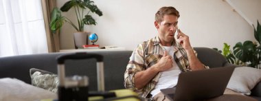 Kızgın bir adamın portresi, hayal kırıklığına uğramış gibi görünüyor, cep telefonuyla konuşuyor, dizüstü bilgisayar ve bavulla oturuyor. Turizm ve halk konsepti