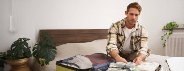 Genç yakışıklı sakallı adamın portresi, tatile çıkan bir turist, giysilerini bavula bağlıyor, tatile çıkıyor, iş gezisine çıkıyor, yatak odasında oturuyor..