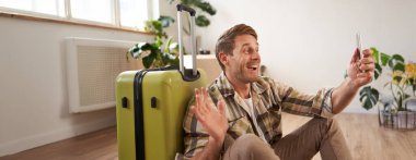 Bavullu neşeli gülen adam, akıllı telefon kullanarak görüntülü sohbetler, selfie çekiyor, tatile çıkıyor..