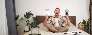 Neşeli, mutlu bir turistin portresi, uçak biletleri ve küreyle oturan bir adam, dünyayı dolaşmak için bavulunu hazırlıyor, tatile çıkıyor, tatilini heyecanla bekliyor..