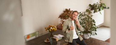 Ofisteki yakışıklı mutlu adamın portresi, ortak çalışma alanında oturan, kameraya bakan, gülümseyen ve gülen, cep telefonuyla konuşan, akıllı telefon kullanan, müşterinin telefonuna cevap veren adam..