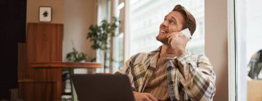 Genç işadamının portresi, şehirdeki kahve dükkanından uzaktan çalışan, dizüstü bilgisayarlı sandalyede oturan, bir telefona cevap veren, cep telefonuyla konuşan.