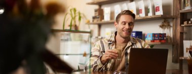 Genç işadamının hayat tarzı portresi, kafede oturan, kahve içen ve dizüstü bilgisayar kullanan, çevrimiçi proje üzerinde çalışan, dijital göçebe, uzaktan kumandalı bir işi var..