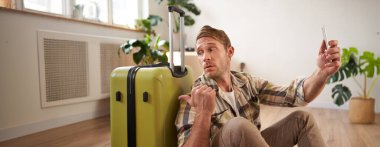 Elinde bavulla gülümseyen yakışıklı bir adamın portresi, bavulla selfie çekmesi, sosyal medyada tatile çıkmakla ilgili yazılar yazması. Turizm ve blog kavramı