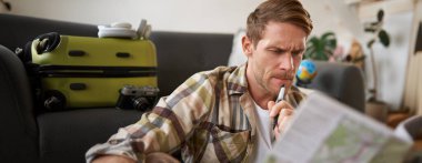 Ciddi yüzü olan bir adam, seyahat haritasına bakıyor, tatil planlıyor, tatile çıkıyor. Seyahat konsepti