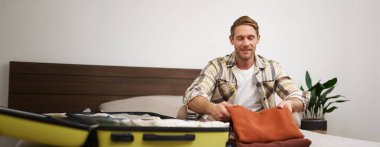 Yakışıklı genç bir adamın portresi, otel odasında bavulları boşaltan turist, tatilde pansiyonda kalan, seyahat eden, yatakta bavullarla oturan..