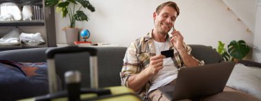 Gülümseyen adamın portresi, turist rezervasyon oteli, telefondan onay, kredi kartı ve dizüstü bilgisayar..