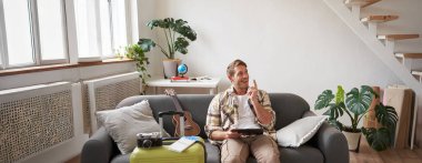 Oturma odasında elinde tabletle oturan genç adamın portresi bavulunu hazırladı ve iki uçak bileti aldı. Yurtdışına gitmeye hazırlanıyor, tatile çıkıyor..