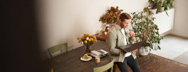 Genç yöneticinin portresi, masada oturan, dizüstü bilgisayarı tutan, ekrana odaklanmış görünen, proje bilgilerini okuyan, iş verilerini kontrol eden, ofiste çalışan ya da ortak çalışan.