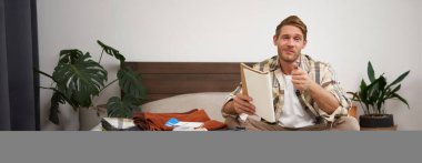 Bavullu bir adamın portresi, tatil için otururken ve eşyalarını toplarken, tatil için eşya listesini kontrol ederken, not alırken, not defterine not alırken. Yaşam tarzı ve turizm konsepti