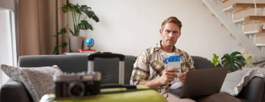 Dizüstü bilgisayarı olan ciddi bir adamın portresi, iki uçuş bileti tutuyor, kaşlarını çatıyor ve endişeli sinirli bir ifadeyle kameraya bakıyor. Turizm ve halk konsepti