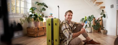 Yakışıklı genç bir adamın portresi, bavuluyla oturan bir turist, elinde pasaport ve uçak biletleri, tatile çıkıyor..