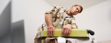 Genç bir adamın portresi, gezgin tatile çıkıyor, bavulunu ütülüyor, iç çamaşırlarını itmeye çalışıyor, bavullarını kapatıyor, tatil için bir sürü şey hazırlamaya çalışıyor. Turizm konsepti