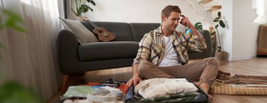 Paniklemiş bir adamın portresi, bavul hazırlıyor, stresli ve endişeli görünüyor, tatilde ne getireceğine dair hiçbir fikri yok..