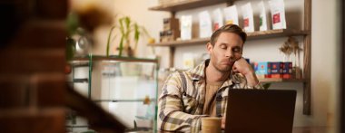 Sıkılmış serbest yazar portresi, dijital göçebe kafeteryada dizüstü bilgisayarla oturuyor, yumruğuna yaslanıyor, can sıkıntısıyla bilgisayar ekranına bakıyor, kahve içiyor, işini yapıyor..