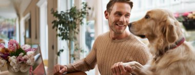 Yakından bakınca akıllı köpeğin portresi sahibine patisini uzatıyor. Evcil hayvan dostu bir kafede oturan altın av köpeğiyle yakışıklı bir adam..