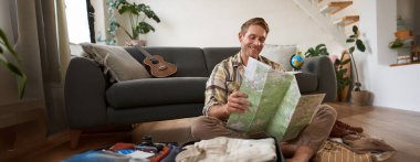 Yakışıklı genç adamın portresi, bavullu gezgin, kağıt haritaya bakıyor, tatilde nereye gideceğini seçiyor, tatile gidiyor, güzergahı seçiyor..