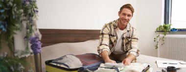 Genç yakışıklı sakallı adamın portresi, tatile çıkan bir turist, giysilerini bavula bağlıyor, tatile çıkıyor, iş gezisine çıkıyor, yatak odasında oturuyor..