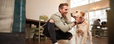 Mutlu genç adamın portresi Golden Retriever 'ıyla kafeye giriyor. Evcil hayvan dostu kafede köpek besleyen yakışıklı adam..