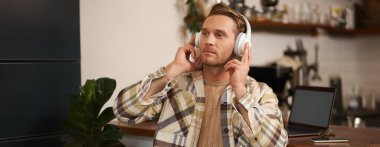 Yakışıklı mutlu adamın portresi, serbest çalışan ve kablosuz kulaklıkla müzik dinleyen, kafede sandalyesinde dans eden, kulaklıkla en sevdiği şarkıyı dinleyen..