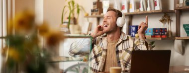 Yakışıklı mutlu adamın portresi, serbest çalışan ve kablosuz kulaklıkla müzik dinleyen, kafede sandalyesinde dans eden, kulaklıkla en sevdiği şarkıyı dinleyen..