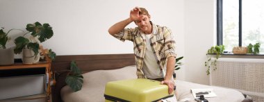 Giysilerle dolu bavulu kapatmaya çalışan bir adamın portresi, bayram için bavul hazırlama çabası, uzun bir tatile çıkma. Turizm ve seyahat acentası kavramı